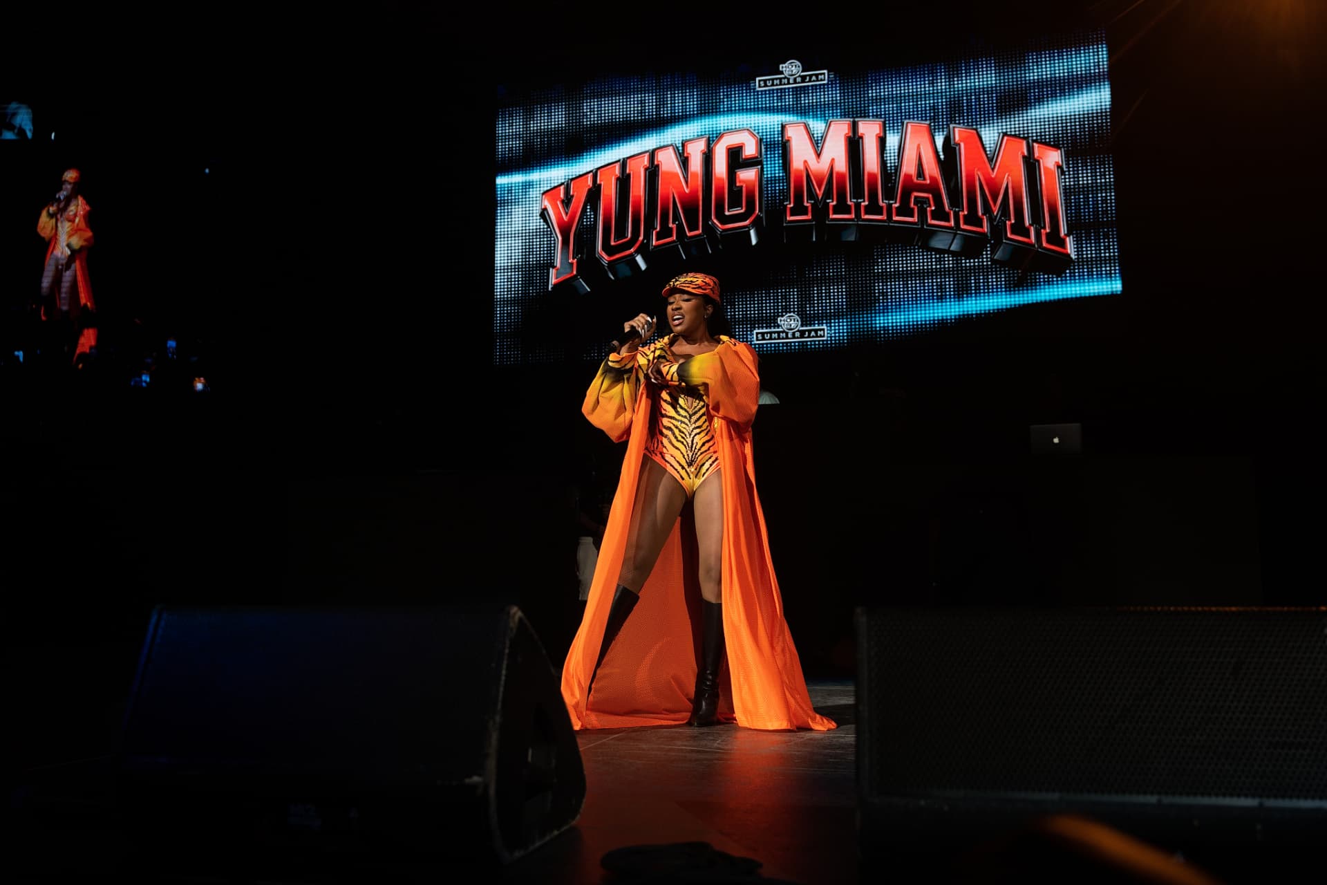 Yung Miami on stage in tiger bodysuit and orange cape